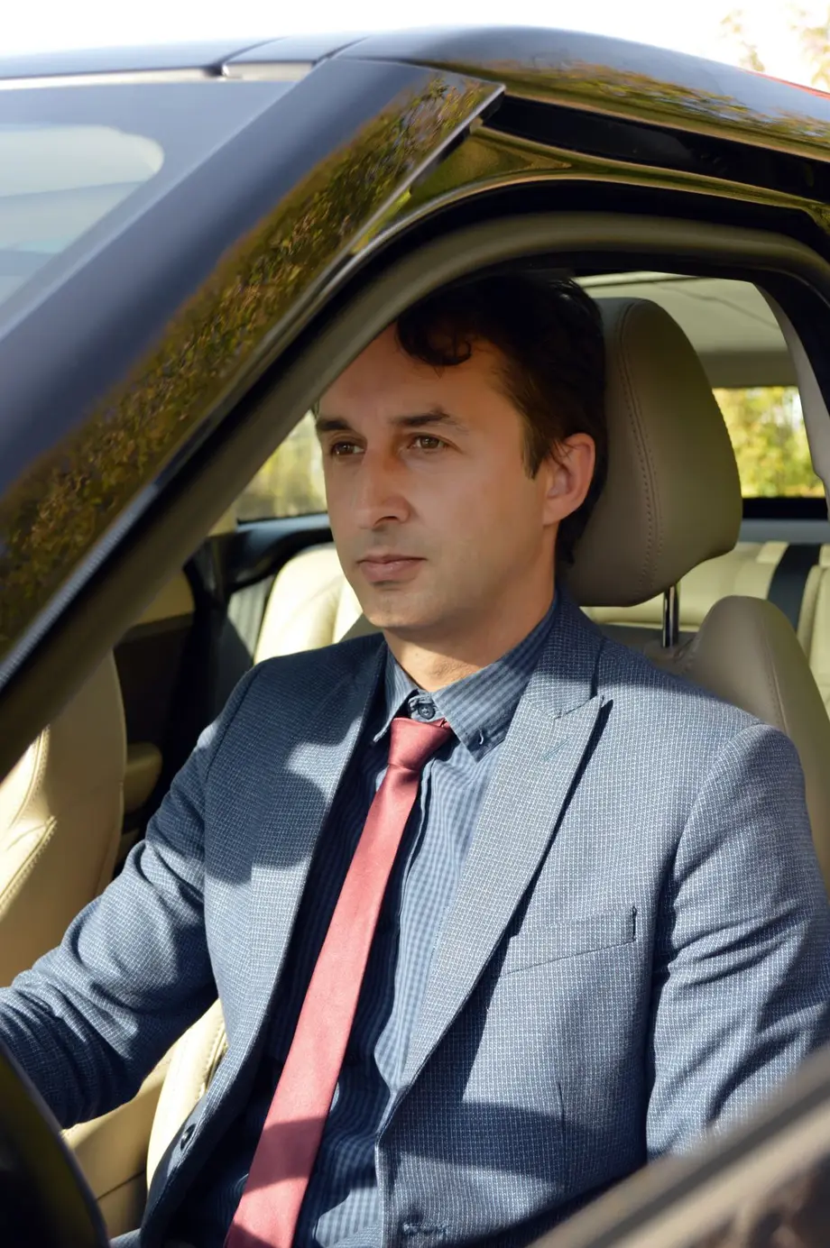 A licensed private hire driver in a suit at the wheel of an executive saloon with a cream leather interior