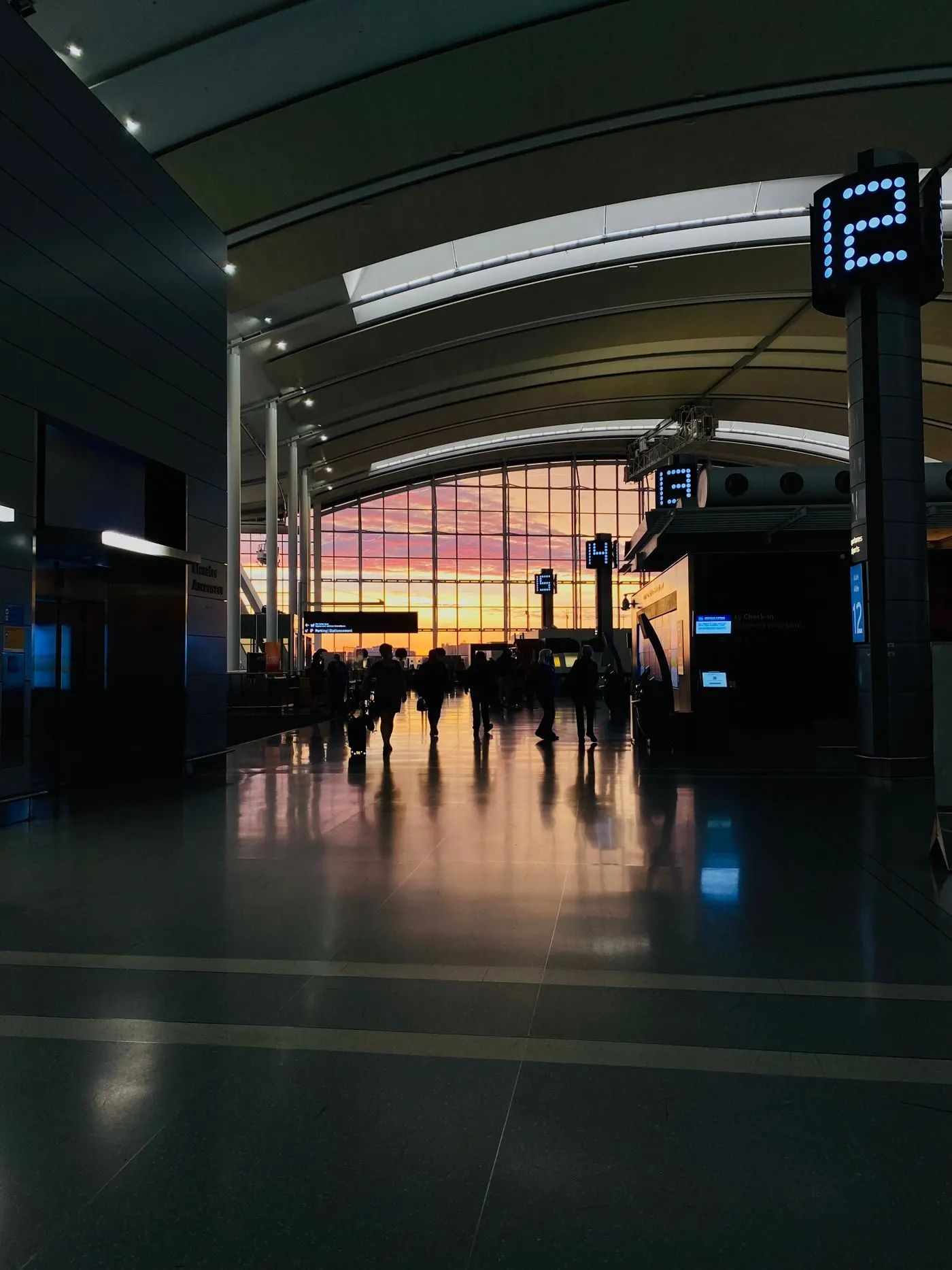 Travellers walking through an airport terminal concourse at dawn with orange light coming through the glass wall